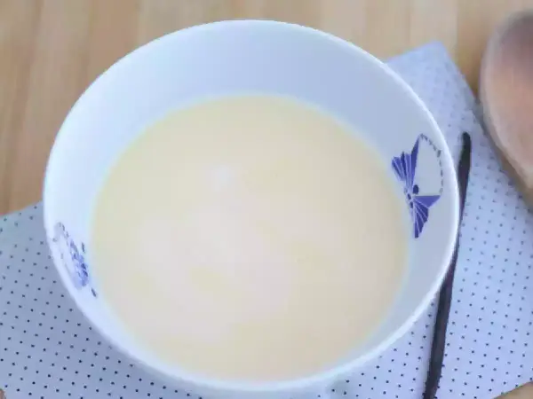 En skål med krämig vaniljsås, perfekt för ditt vaniljsås recept. En vaniljstång ligger bredvid.