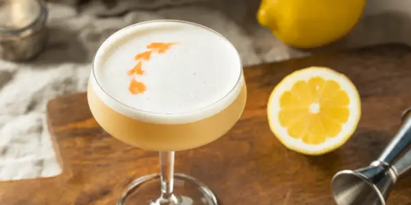 En läcker sifon drink med skummig topp, garnerad med orange mönster. Citroner och en jigger ligger bredvid.